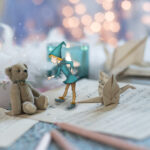 Ours en peluche posé sur des feuilles de musique, accompagné d’un personnage illustré dans une scène miniature.