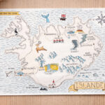 Carte illustrée de l’Islande représentant un itinéraire de road trip, posée sur une surface en bois clair.